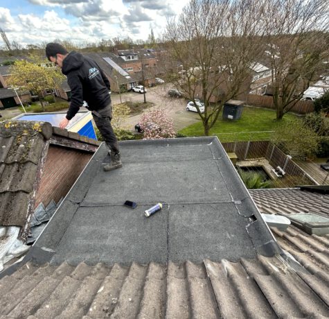 Een vakman van LS Dakspecialist brengt bitumen dakbedekking aan op een plat dak, uitgerust met veiligheidskleding en gebruikmakend van een brander voor een optimale hechting.