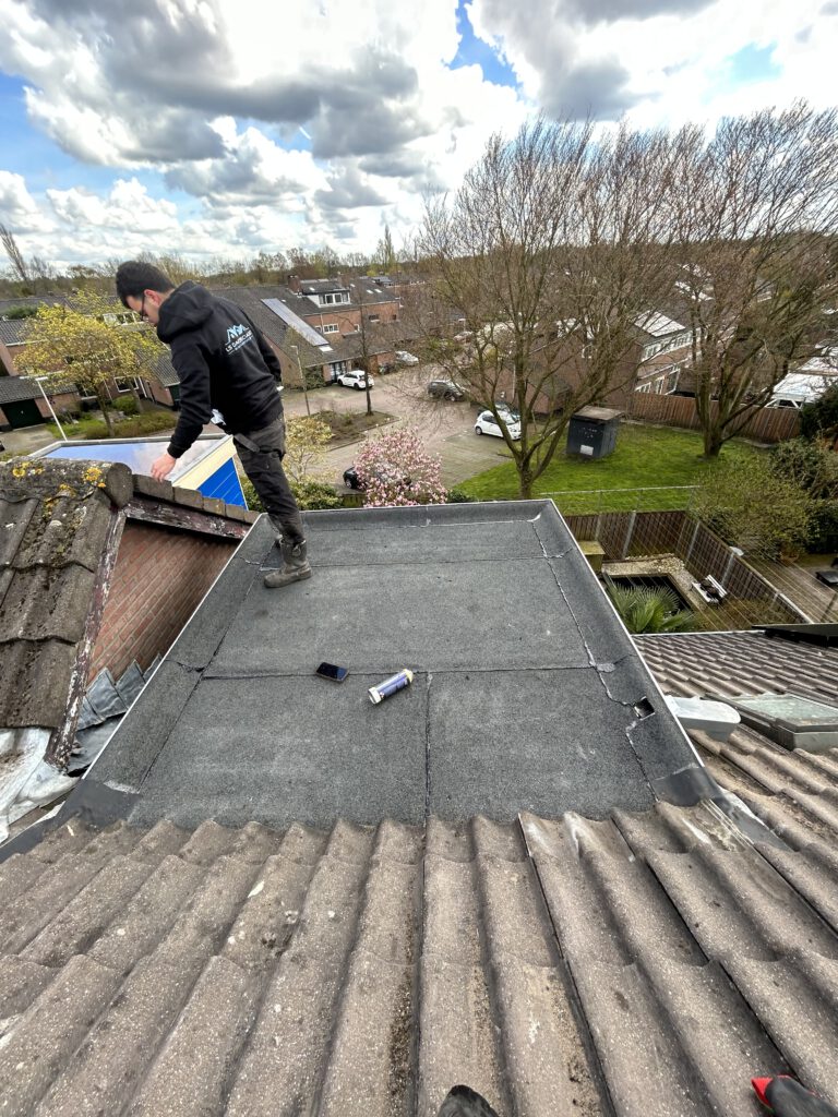 Een vakman van LS Dakspecialist brengt bitumen dakbedekking aan op een plat dak, uitgerust met veiligheidskleding en gebruikmakend van een brander voor een optimale hechting.