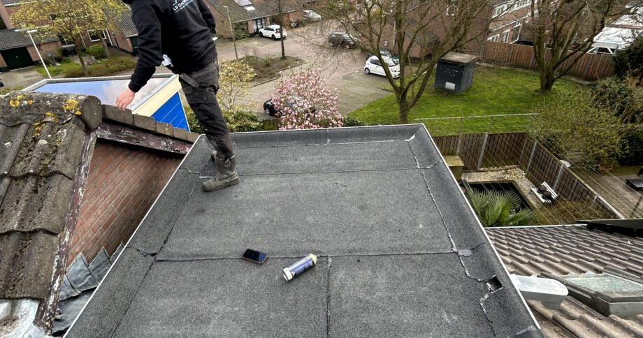 Een vakman van LS Dakspecialist brengt bitumen dakbedekking aan op een plat dak, uitgerust met veiligheidskleding en gebruikmakend van een brander voor een optimale hechting.