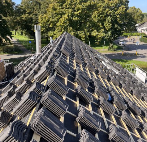 Stapels dakpannen liggen netjes opgesteld naast een dak voorbereid met dakfolie en panlatten, klaar om geïnstalleerd te worden