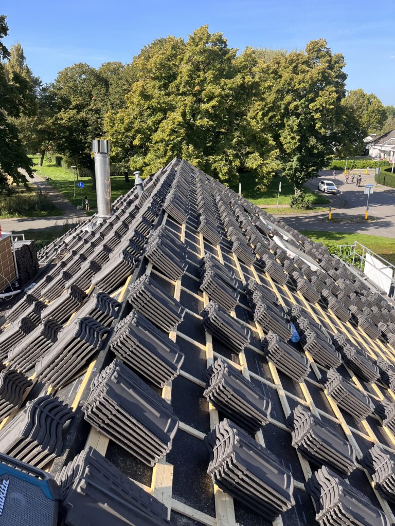 Stapels dakpannen liggen netjes opgesteld naast een dak voorbereid met dakfolie en panlatten, klaar om geïnstalleerd te worden