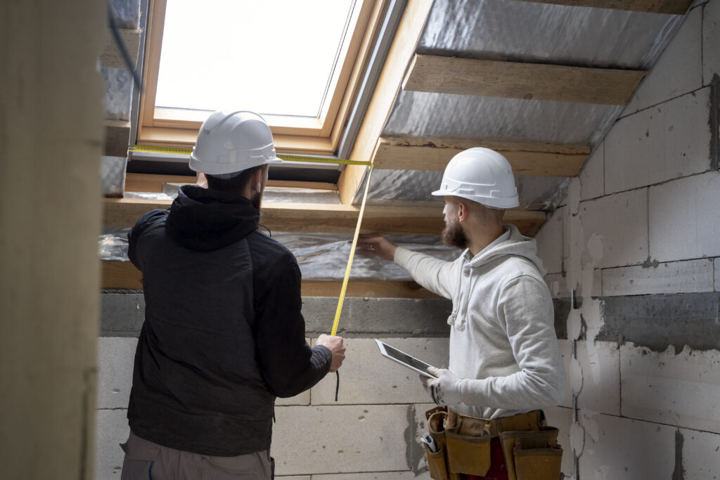 Een professionele dakisolatiespecialist van LS Dakspecialist installeert isolatiemateriaal onder het schuine dak van een woonhuis, gekleed in veiligheidskleding en met gebruik van specifieke gereedschappen.